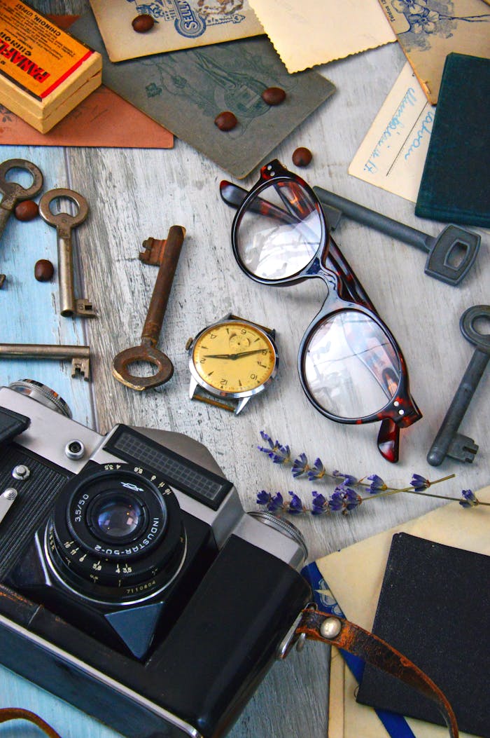 A stylish flat lay featuring vintage camera, keys, watch, and glasses on a wooden table.