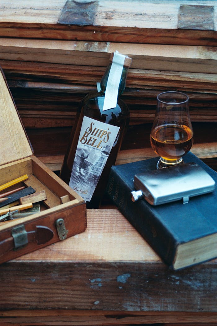A vintage setup featuring whiskey, a glass, flask, and open wooden box on a rustic background.